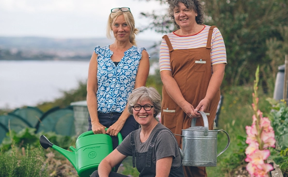 Three women with watering cans smiling