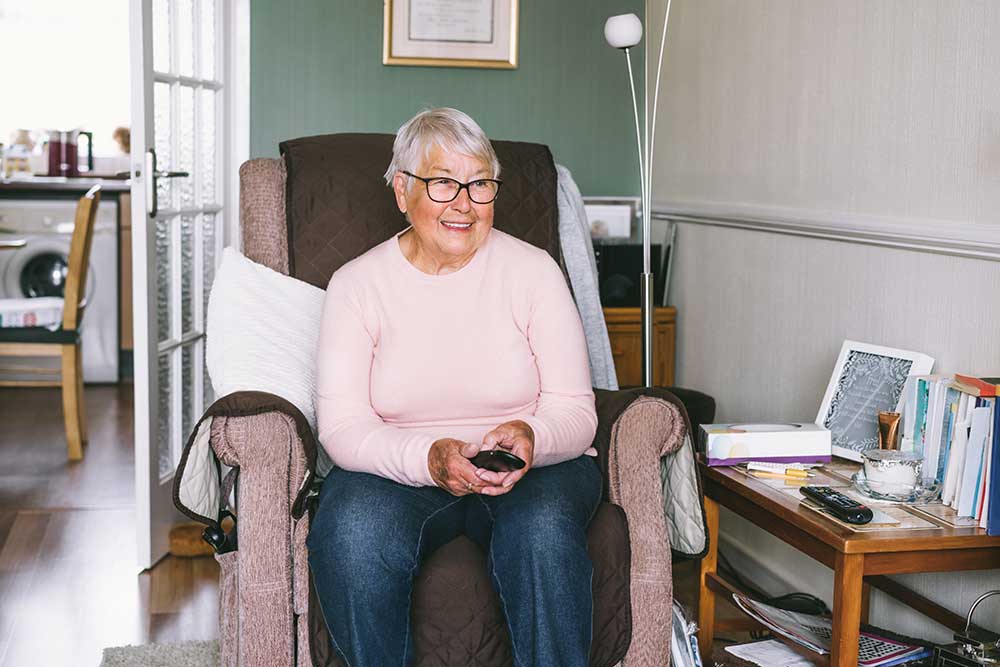 Pensioner sat in a chair holding a television remote