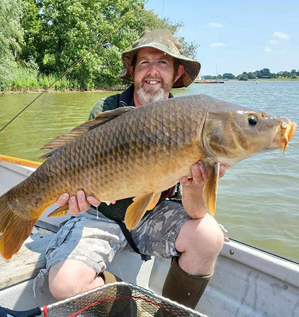 Angler in a fishing boat holding a carp fish